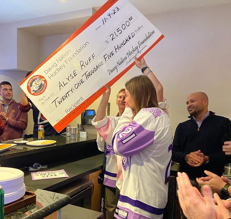 alyse receiving check for cancer treatment from dawg nation hockey foundation